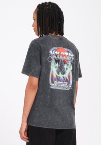 Czarny, przetarty, oversize t-shirt z wielokolorową grafiką na plecach, z abstrakcyjnymi wzorami i tekstem. Krótkie rękawy, okrągły dekolt.