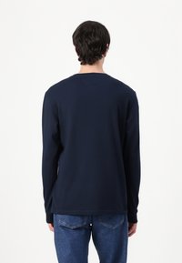 Marineblå langermet skjorte med rund hals, laget av mykt stoff, har et enkelt design uten grafikk eller dekorasjoner.