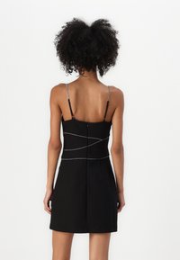 Svart klänning med kroppsnära överdel och utsvängd kjol. Har metallkedjestrarpar och dekorativ silverstickning över ryggen.