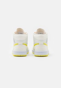 Pair of white mid-top sneakers with yellow accents, textured leather, and white midsoles, shown from the back on a white background.