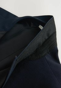 Marineblazer mit wollgefüttertem Kragen; glattes Innenfutter, strukturierte Form und detaillierte Stickerei entlang des Kragenrandes.