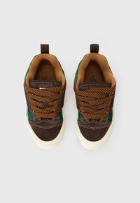 Pár hnědých a zelených volnočasových tenisek na šněrování s bílými gumovými špičkami, zobrazený zvrchu na bílém pozadí.