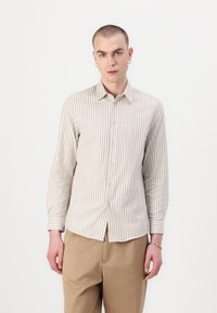 Rstripete langermet skjorte i lys beige og hvitt, laget av mykt stoff, med knappeåpning foran og mansjetter, paret med beige bukser.