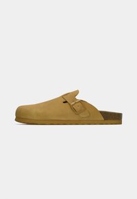 Παπούτσι στυλ κλογκ από ανοιχτό καφέ καστόρι, με ένα ενιαίο ρυθμιζόμενο λουράκι με αγκράφα, υφή σόλας φελλού και στρογγυλεμένο σχέδιο μύτης.