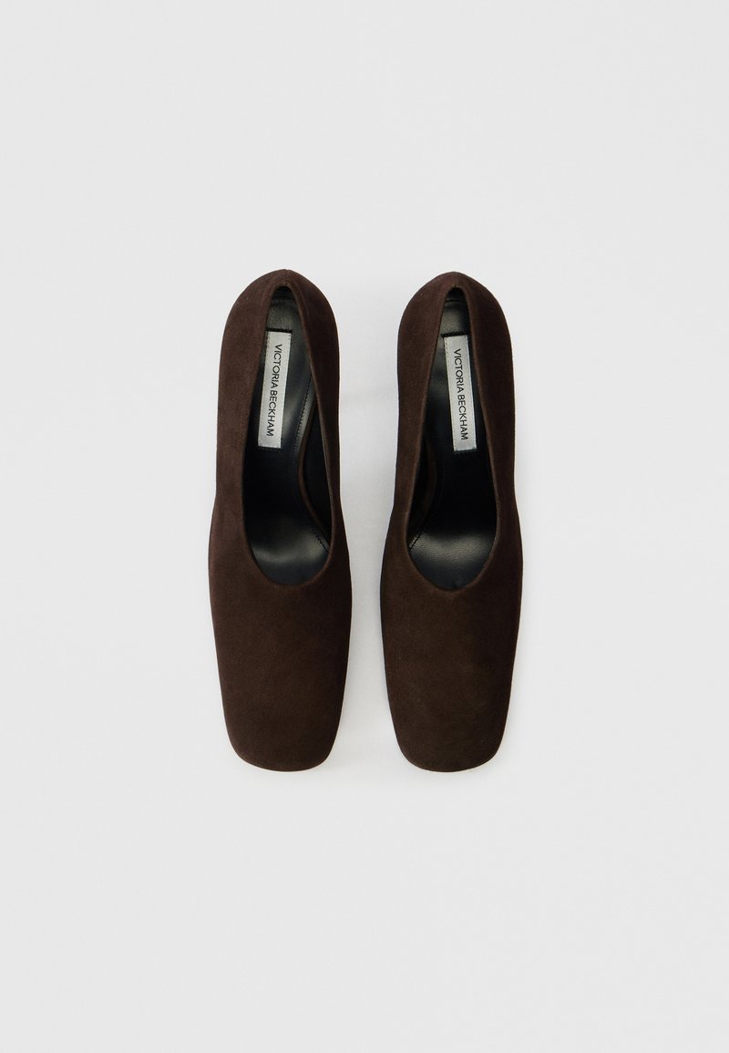 Décolleté in camoscio marrone con punta quadrata, tacco elevato e fodera interna liscia. Presenta un design con ritagli e un branding minimale sulla soletta.