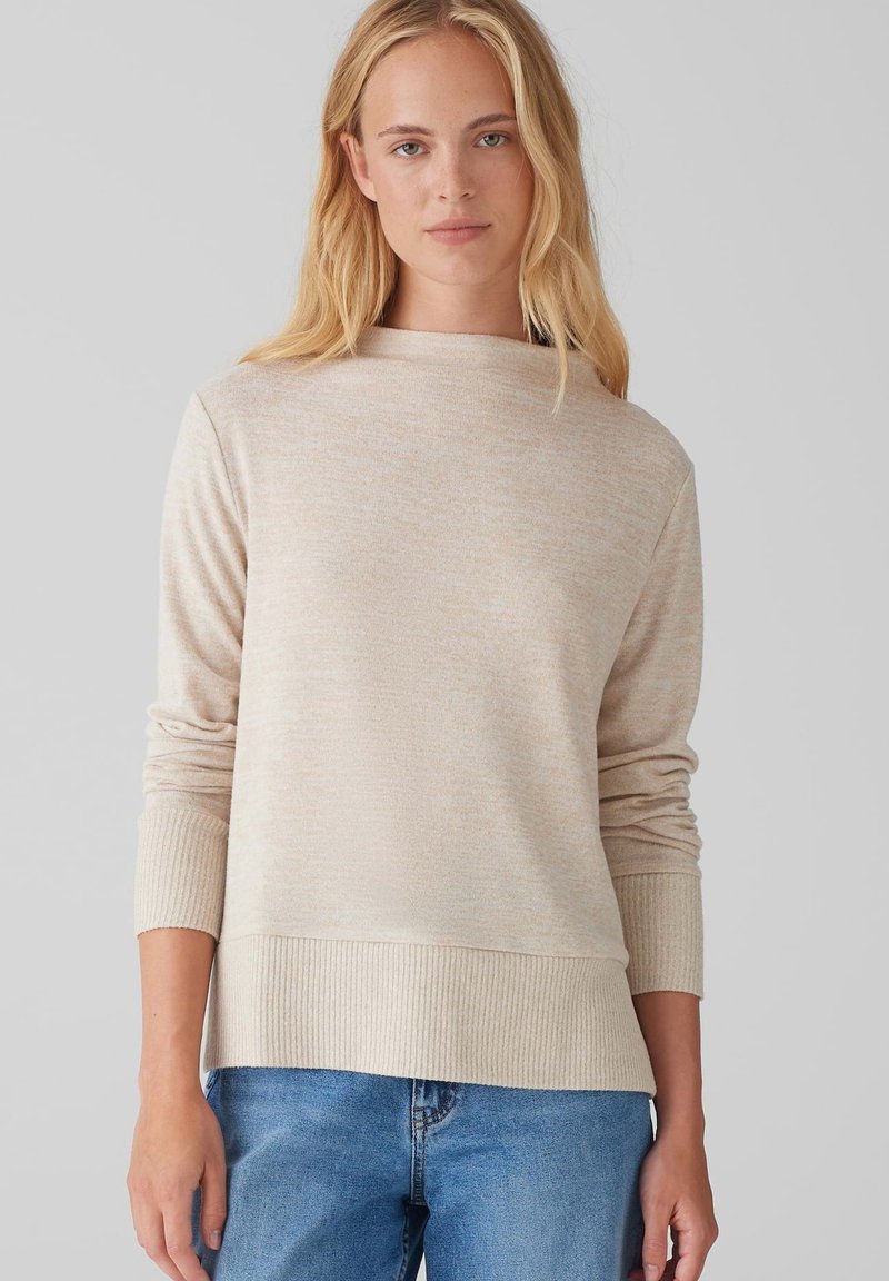 Beige sweater with a crew neck and ribbed cuffs. Soft texture and a relaxed fit, paired with light blue jeans.