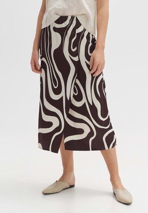 Bruin en wit gemêleerde midi rok met een relaxte pasvorm, voorzien van een splitzoom en een elastische tailleband, gecombineerd met lichtgekleurde platte schoenen.