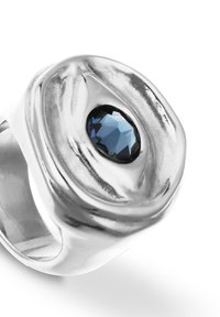 Anillo de plata con un diseño ondulado y texturizado, con una piedra preciosa azul facetada central, enmarcada en un engaste negro.