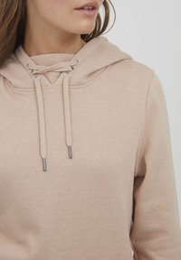 Ljusrosa hoodie med en stor huva, featuring metallöglor och matchande dragsnören. Slät textur, avslappnad design.