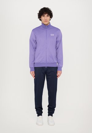 Purple zip-up jacket with high collar, paired with navy sweatpants. The jacket features an EA7 logo on the chest and ribbed cuffs.
