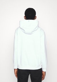 White hoodie with a smooth texture, adjustable drawstring hood, and ribbed cuffs. Features a minimalist design with subtle branding on the back.