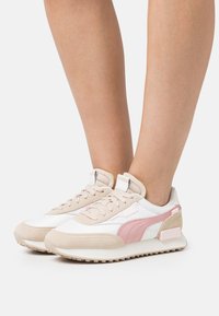 Sneakers leggeri in rete bianca e morbido suede beige, caratterizzati da una striscia accentuata rosa, dettagli texturizzati e un design con suola imbottita.