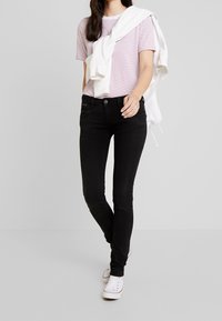 Czarne skinny jeans z denimu, połączone z jasnoróżową koszulką w białe paski i białymi trampkami. Na ramionach założona jest biała bluza.