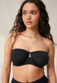 Zwarte strapless beha met een soepele textuur, gestructureerde cups en een sluiting aan de voorkant. Minimalistisch ontwerp met versterkte stiksels.