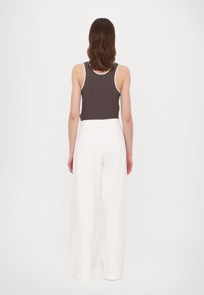 Brūns topiņš ar baltu apdari, kombinēts ar brīvi pieguļošām, augstas jostasvietas baltām biksēm. Gluda auduma, minimālistisks dizains.