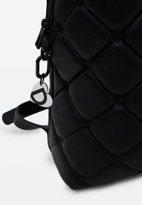 Czarny skórzany plecak z pikowanym wzorem, wyposażony w metalowy brelok w kształcie serca, zamek błyskawiczny oraz regulowany pasek.