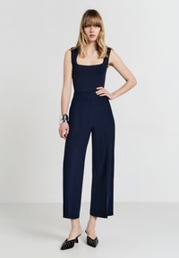 Tuta senza maniche di colore blu navy con scollatura quadrata e pantaloni a gamba larga. Realizzata in un tessuto morbido, presenta un corpetto aderente e linee pulite.