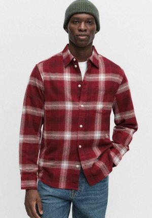 Röd och vit rutig skjorta med knapp, klassisk krage, lång ärm och bröstficka, i kombination med blå jeans och en grön stickad mössa.