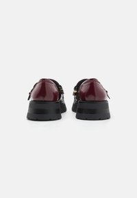 Burgundy patent leather shoes with a chunky black platform sole, featuring a smooth texture and minimal hardware detailing.