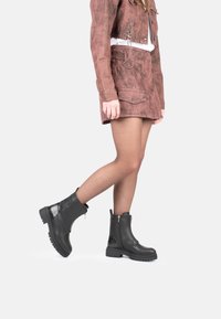 Botas de tobillo de cuero negro con un panel texturizado y cremallera lateral, con suela gruesa y un acabado suave. Adecuadas para diversas indumentarias.