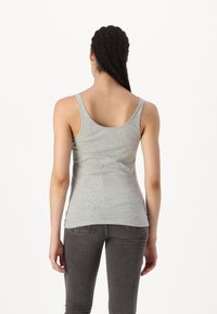 Camiseta de algodón gris sin mangas con escote en la espalda y tirantes anchos, de forma ajustada y con una textura suave. Combinada con pantalones gris oscuro.