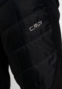 Sección de chaqueta acolchada negra con el logotipo CMP bordado en blanco en un panel de tejido acolchado.