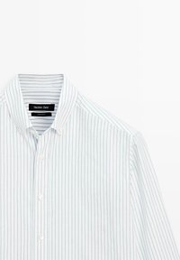 Camicia bianca con righe verticali azzurre, in tessuto di cotone, colletto a punta e piccolo logo etichetta sul colletto.