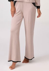 Jasnoróżowe dzwony piżamowe z prążkowanego materiału, z czarną koronką na końcu i kieszeniami, o luźnym kroju.