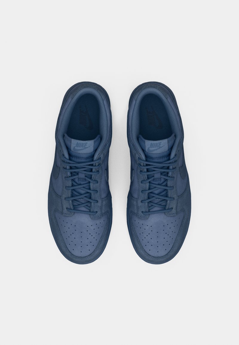 Zapatillas deportivas azul de ante con una superficie texturizada, puntera perforada y cordones a juego. Presenta un logotipo sutil en la lengua y en el costado.