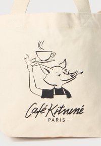 Beige lerret totebag med en svart illustrasjon av en rev som holder en kaffekopp, med teksten "Café Kitsuné Paris" under.