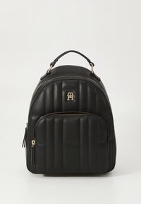 Mochila preta em couro acolchoado com ferragens douradas, formato arredondado, alça superior e bolso frontal com fecho de correr. Apresenta um logótipo na parte da frente.