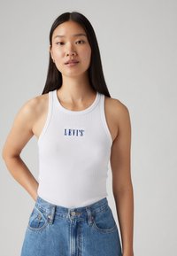 Balta grills marškinėliai su mėlyna "LEVI'S" logotipu, derinami su mėlynais džinsiniais šortais, aukšta juosmens linija. Paprastas ir prigludęs dizainas.