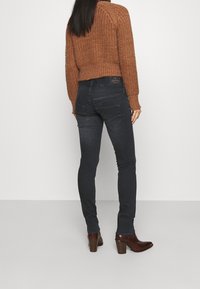 Tummansiniset kapeat farkut, joissa on sileä pinta ja korkea vyötärö, yhdistettynä ruskeaan neulepaitaan, käytetty ruskeiden korkokenkien kanssa.