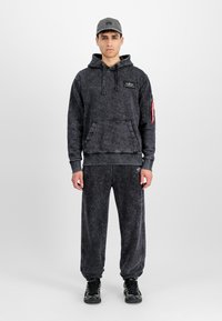 Black tie-dye hoodie with front pocket and logo patch, paired with matching joggers featuring elastic cuffs and side detailing. Worn with black shoes.