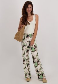 Witte gebreide tanktop gecombineerd met losse, gestreepte broek in groen, zwart en wit. Gevlochten mandtas en beige gevlochten schoenen.