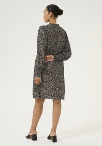Robe à manches longues dans un motif abstrait gris et noir, dotée d'une coupe décontractée et d'un tissu doux. Associée à des mules noires à talons.