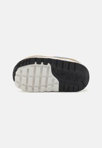 Podeszwa sneakersów z fakturowaną białą wkładką, sztywną czarną gumową bieżnią i brązowym akcentem z zamszu; szczegółowe logo na pięcie.
