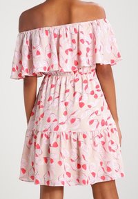 Vestido de tirantes caídos en tela rosa claro con patrones de hojas rojas, con un escote con volantes y un dobladillo de capas. Cintura elástica para un mejor ajuste.