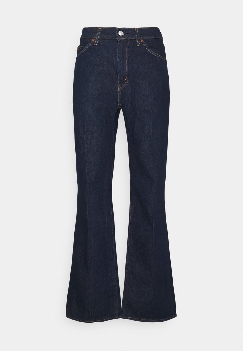 Vaqueros acampanados de un azul oscuro, fabricados en denim, con una cintura alta, bolsillos frontales y herrajes de botón de latón. Textura suave con costuras amarillas.