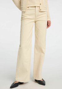 Krémové volné džíny z denimu, které mají pět kapes, vysoký pas a čistý lem. V kombinaci s černými botami.