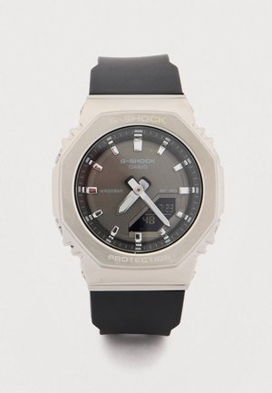 G-Shock horloge met een grote, ronde metalen kast, grijze wijzerplaat, zwarte rubberen band en lichtgevende wijzers. Heeft een digitaal display en is waterbestendig.