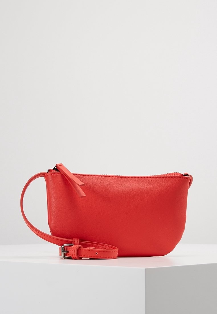 Červená kožená taštička s hladkým povrchem, se zipovým uzávěrem a odnímatelným náramkem na zápěstí. Obsahuje malou dekorační pásku na zipu.