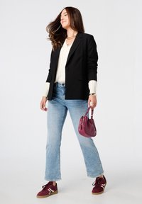Zwarte blazer over een crèmekleurige trui, lichtblauwe jeans en bordeauxrode sneakers. Draagt een kleine, ronde roze tas. Casual outfit.