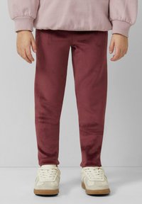 Burgundy, velvet-like leggings with a smooth texture and a fitted shape, paired with white and beige sneakers. Cozy, casual look.