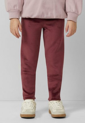Burgunderfarbene, samtartige Leggings mit glatter Textur und eng anliegender Form, kombiniert mit weißen und beigen Sneakers. Gemütlicher, lässiger Look.