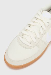 Baskets en toile beige clair avec une surface texturée, logo blanc et lacets ronds ; dotées d'une semelle en caoutchouc et d'accents cousus.