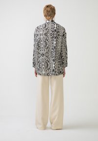 Camicia a maniche lunghe con motivo bianco e nero, con chiusura a bottoni e vestibilità rilassata, abbinata a pantaloni ampia crema.