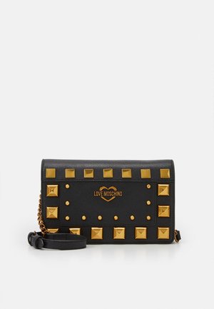 Clutch de cuero sintético negro texturizado con tachuelas en forma de pirámide doradas y una correa de cadena. Presenta una placa de logo dorada en el centro.