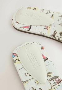 Deux semelles en tissu blanc avec des imprimés colorés sur le thème de la plage et des coussinets de talon blancs rembourrés embossés « NEXT Forever Comfort ».