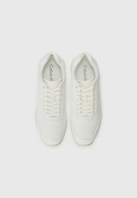Sneaker bianche con superficie texturizzata, caratterizzate da motivi circolari, chiusura con lacci e branding "Calvin Klein" sulla linguetta e sulla soletta.